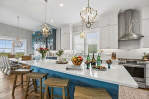 Une cuisine moderne dotée d’un grand îlot central, d’appareils électroménagers en acier inoxydable et de luminaires suspendus.