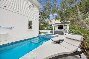 Una piscina con sillones de descanso, una casa blanca y un árbol.