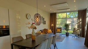 A modern kitchen with a dining area, a clock on the wall, and a large window with curtains. - L-cube Hottub 4+2 (Maarn)