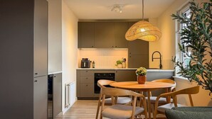 A modern kitchen with wooden cabinets, a dining table with chairs, and a hanging light fixture. - Stunning 2 Bed, 2 Bath Apartment with Parking (Duntocher)