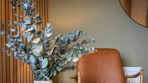 A room with a brown leather chair, a wooden table, and a vase with a geometric design. - Stunning 2 Bed, 2 Bath Apartment with Parking (Duntocher)