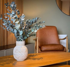 A room with a brown leather chair, a wooden table, and a vase with a geometric design. - Stunning 2 Bed, 2 Bath Apartment with Parking (Duntocher)