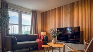 A modern living room with a sofa, a coffee table, a TV, and a wooden wall paneling. - Stunning 2 Bed, 2 Bath Apartment with Parking (Duntocher)