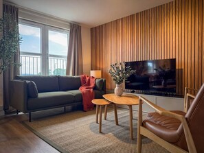 A modern living room with a sofa, a coffee table, a TV, and a wooden wall paneling. - Stunning 2 Bed, 2 Bath Apartment with Parking (Duntocher)