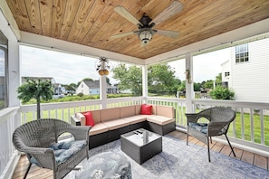 Eine überdachte Terrasse im Freien mit Deckenventilator, Korbmöbeln und Blick auf die Nachbarschaft.