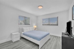 A modern bedroom with a white bed, two bedside tables, a TV, and windows with blinds. - West Brickell #4 Free Parking & Renovated 2BR (Miami)