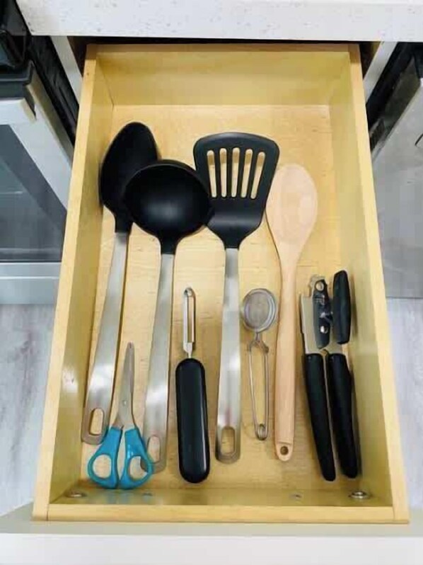 Uma gaveta com diversos utensílios de cozinha, incluindo uma tesoura, uma concha, uma espátula e um ralador.
