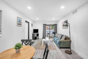 Ein modernes Wohnzimmer mit Sofa, Fernseher, Esstisch und einer Pflanze.