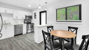 A modern kitchen with white cabinets, stainless steel appliances, and a dining area with a wooden table and black chairs. - West Brickell #3  Minutes to Downtown Miami (Miami)