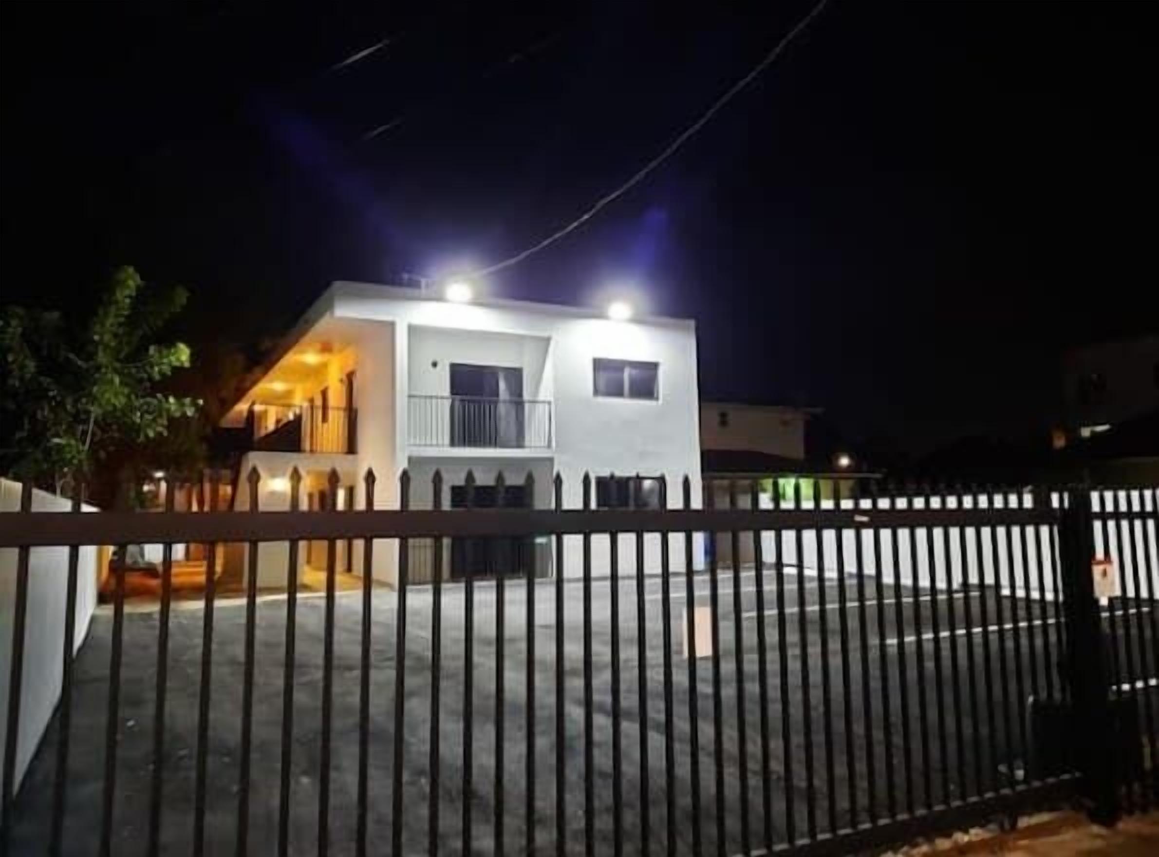 Een modern herenhuis met twee verdiepingen en een omheinde tuin, verlicht door buitenverlichting.