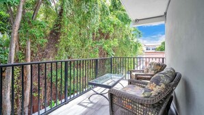 A balcony with wicker furniture, a glass table, and a view of trees and buildings. - West Brickell #3  Minutes to Downtown Miami (Miami)