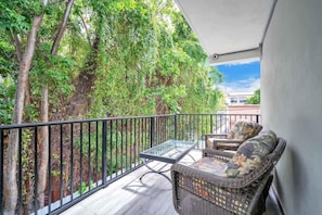 Ein Balkon mit Korbmöbeln, einem Glastisch und Blick auf Bäume und Gebäude.