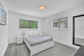Ein Schlafzimmer mit einem Bett, zwei Nachttischen, einem Fenster mit Jalousien und einer Deckenleuchte.