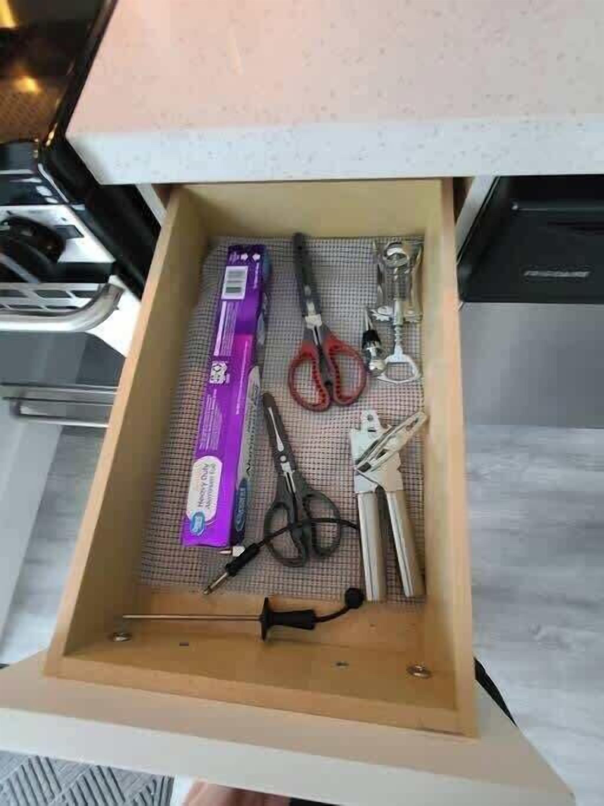 A drawer with a purple box, scissors, a pair of red-handled pliers, and a metal tool.