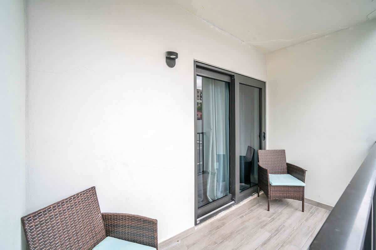 A balcony with two wicker chairs, a sliding glass door, and a light-colored floor.