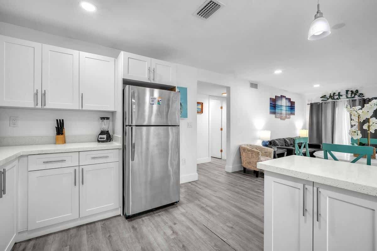 Una cocina moderna con armarios blancos, un refrigerador de acero inoxidable y un comedor con mesa y sillas.