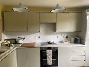 Eine Küche mit weißen Schränken, einem Toaster, einem Wasserkocher und einem Radio. Zwei Pendelleuchten sind angebracht.