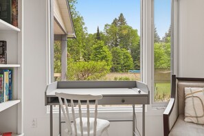 Une pièce comprenant un bureau, une chaise et offrant une vue sur un paysage verdoyant grâce à une grande fenêtre.