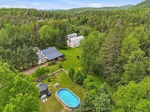 Una casa con piscina, rodeada de un bosque denso y colinas.