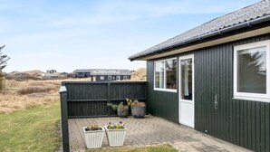 A single-story building with a dark exterior, a front door, and a window. There are two planters with flowers on the front porch. - "Sida" - 400m from the sea by Interhome (Løkken)