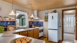 A modern kitchen with a white refrigerator, wooden cabinets, a blue tiled backsplash, and a window with a view. - "Sida" - 400m from the sea by Interhome (Løkken)