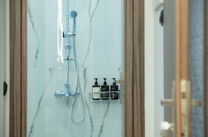 A bathroom with a marble wall, a shower with a handheld showerhead, and a soap dispenser mounted on the wall. - Klitiou 7 Boutique Hotel (Athina)