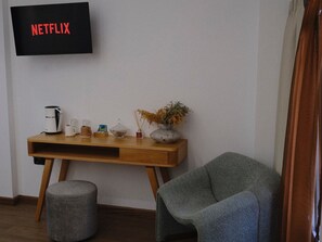 Un salon moderne avec une table basse en bois, un fauteuil gris, un petit pouf et un téléviseur fixé au mur qui affiche « NETFLIX ».