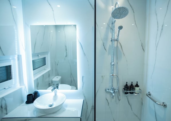 Un baño moderno con un lavamanos de mármol, un cabezal de ducha de mano y una ducha con mampara de vidrio.