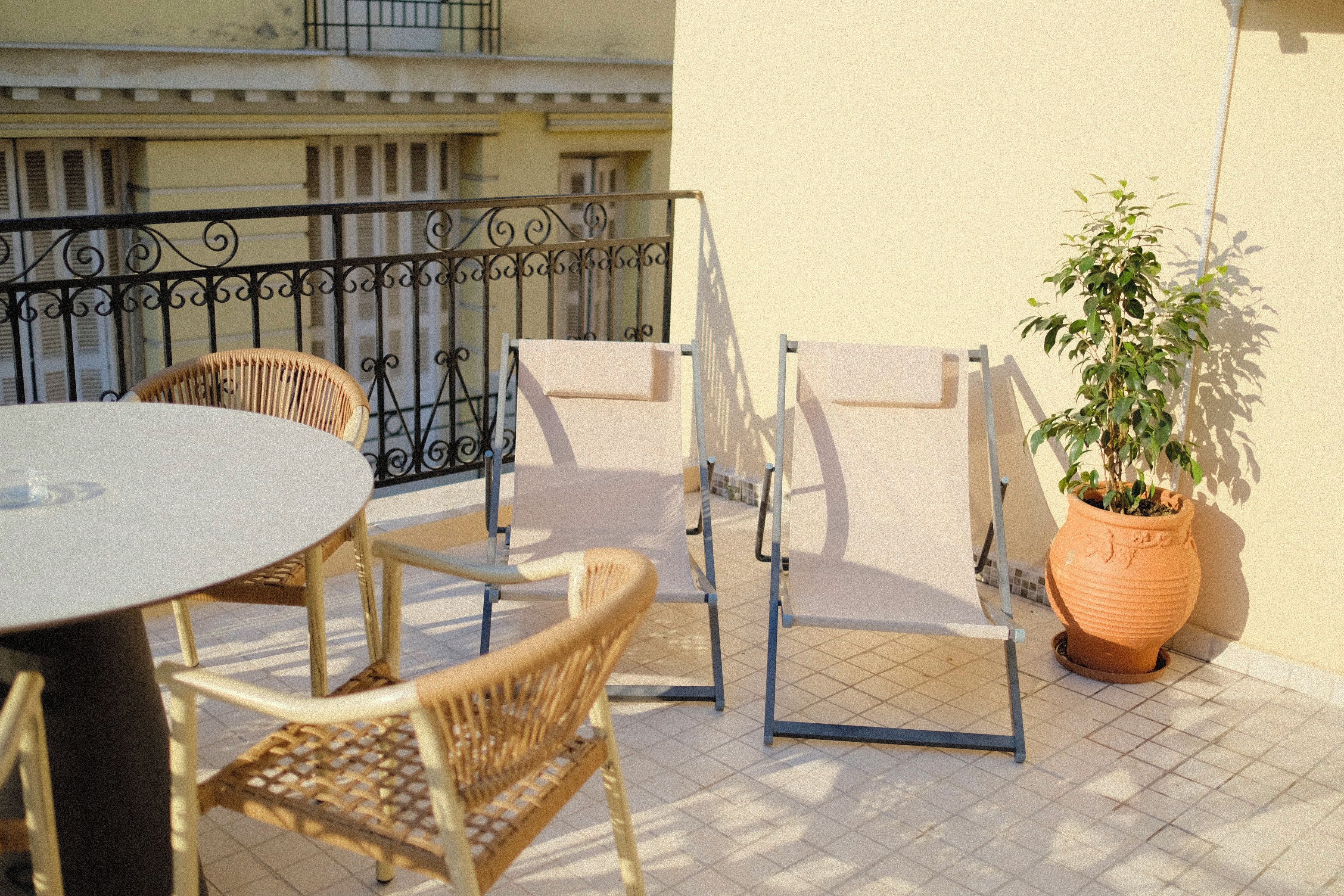 A balcony with a round table, two wicker chairs, a potted plant, and a metal railing.
