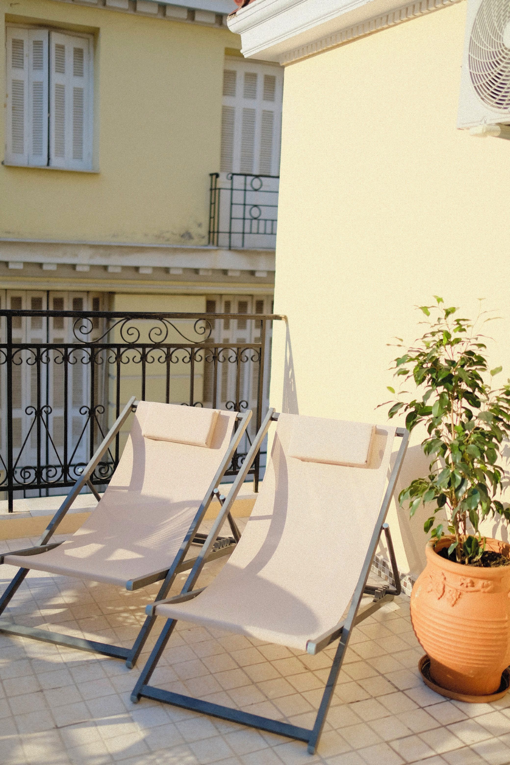 Two sun loungers on a tiled patio with a potted plant beside them.