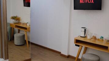 A hotel room with a wooden desk, a coffee maker, a mirror, and a wall-mounted TV displaying 'NETFLIX'.