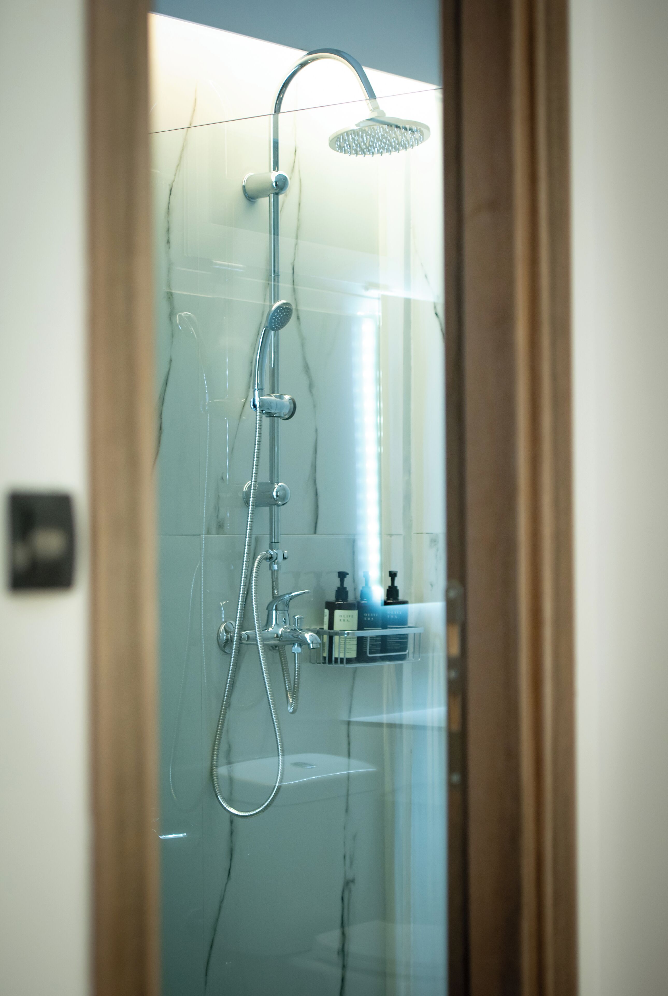 A glass-enclosed shower with a handheld showerhead, a wall-mounted faucet, and a control panel.