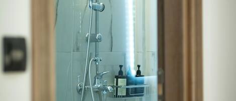 A glass-enclosed shower with a handheld showerhead, a wall-mounted faucet, and a control panel.