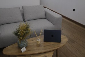 A modern living room with a grey sofa, a wooden coffee table, a vase with dried plants, and a laptop. -  Klitiou 7 Boutique Hotel (Athens)