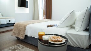 Une chambre d’hôtel moderne, équipée d’un lit, d’une table de chevet avec un plateau de petit-déjeuner, d’un téléviseur fixé au mur et d’une fenêtre avec des rideaux.