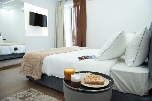 A modern hotel room with a bed, a bedside table with breakfast, a TV on the wall, and a window with curtains. -  Klitiou 7 Boutique Hotel (Athens)