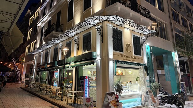 Un immeuble avec un café au rez-de-chaussée, une boulangerie dont la vitrine donne sur la rue, et une moto garée devant.