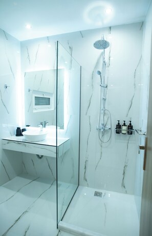 Une salle de bain moderne dotée d’une douche à parois de verre, d’un lavabo en marbre blanc et d’un meuble à pharmacie encastré.