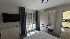 Ein modernes Hotelzimmer mit Bett, Fernseher, Kleiderschrank und einem durch eine Schiebetür einsehbarer Badezimmer.