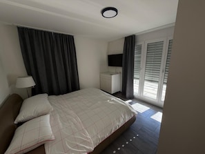 Ein Schlafzimmer mit einem Bett, einem Schreibtisch, einem Fernseher und einem Fenster mit Jalousien.