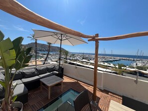 A terrace with a sofa, table, umbrella, and a view of a marina.