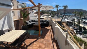 Eine Dachterrasse mit Holzboden, einer Couch, einem Tisch und Blick auf den Hafen und die Berge.