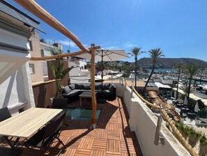 Eine Dachterrasse mit Holzboden, einer Couch, einem Tisch und Blick auf den Hafen und die Berge.