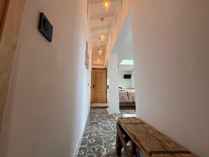 A hallway with patterned flooring, a wooden bench, and hanging pendant lights.
