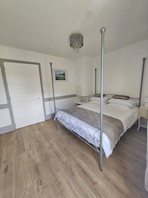 A bedroom with a four-poster bed, a door, a framed picture, and a chandelier.