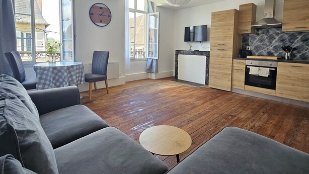 Ein modernes Wohnzimmer mit einer Couch, einem kleinen runden Tisch und einer Küchenzeile mit Holzschränken und einem Fernseher.