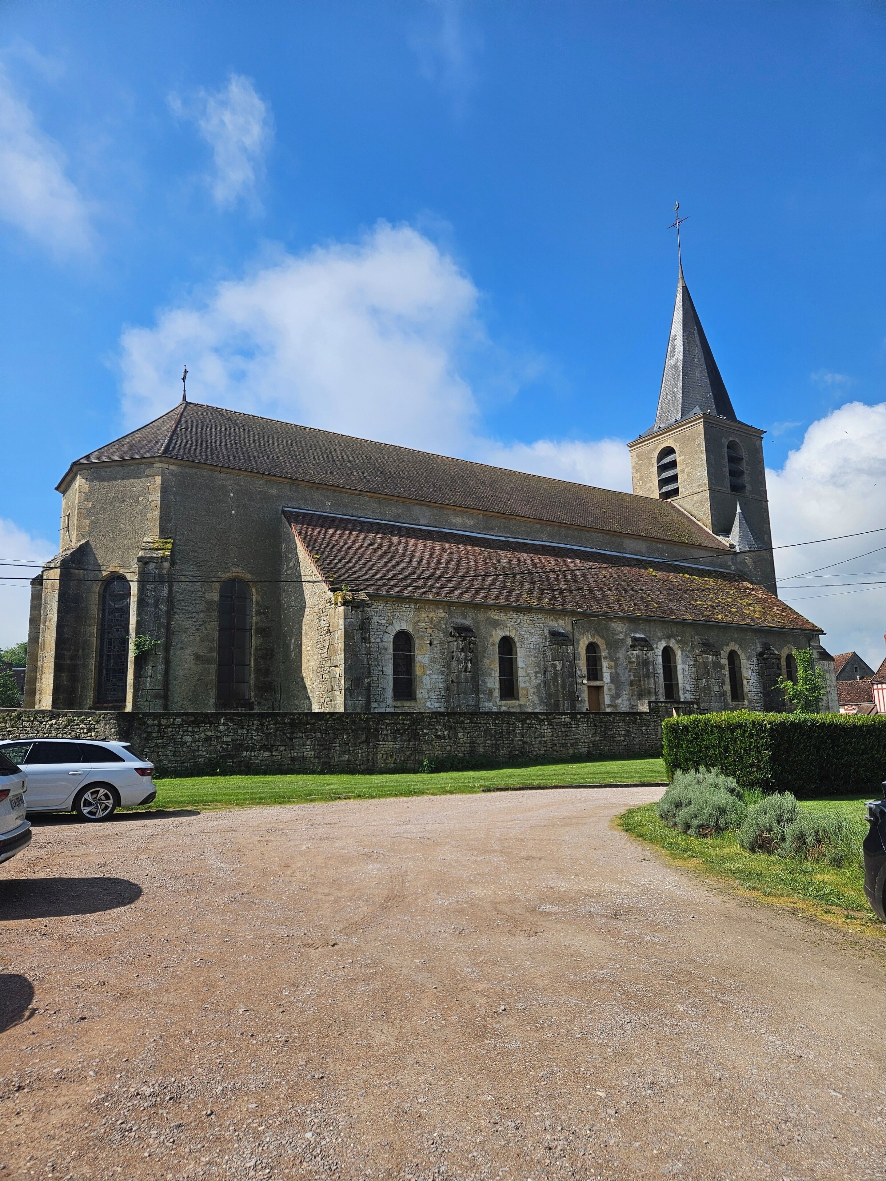 Uma igreja histórica com uma torre imponente, uma entrada de cascalho e um carro estacionado.