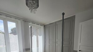 Ein Schlafzimmer mit Bett, einer Kandelaber, einem Kleiderschrank und einem Fenster mit Vorhängen.