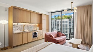 Een moderne hotelkamer met een keuken, een groot raam met uitzicht op de stad, een rode bank en een kleine houten tafel.