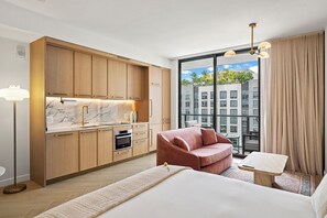 Ein modernes Hotelzimmer mit Küche, einem großen Fenster mit Blick auf die Stadt, einem roten Sofa und einem kleinen Holztisch.